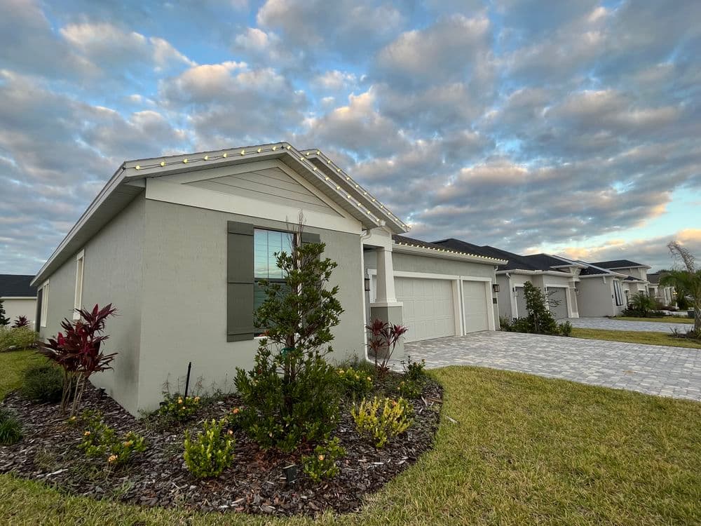 Modern home exterior with landscaped garden under a cloudy sky, featuring a paved driveway.