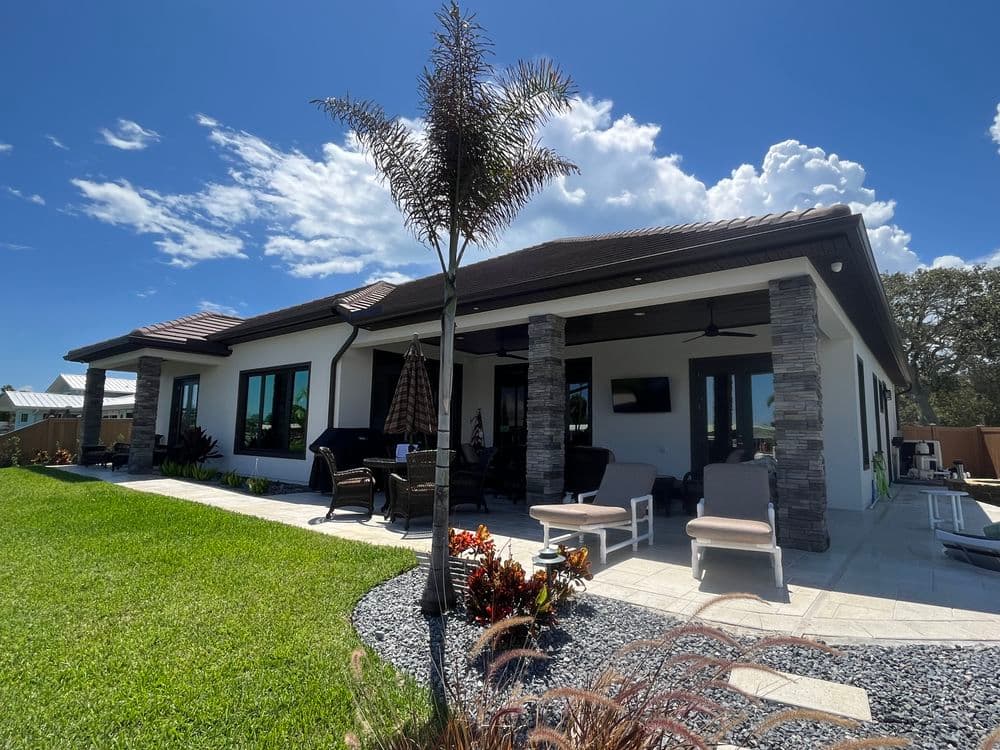 Modern single-story house with stone accents, lush lawn, and patio furniture under blue sky.