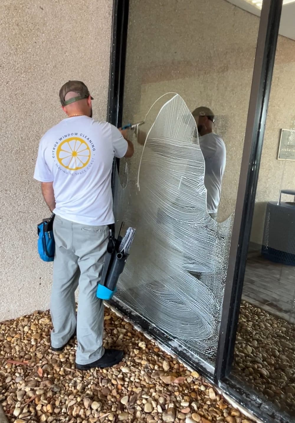 Window cleaner washing a large glass surface with a squeegee and cleaning solution.