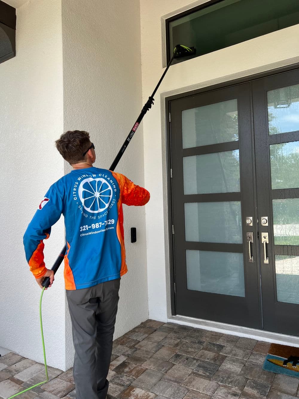 Man using a pole to clean a window on a modern home's exterior. Brightly colored work shirt.