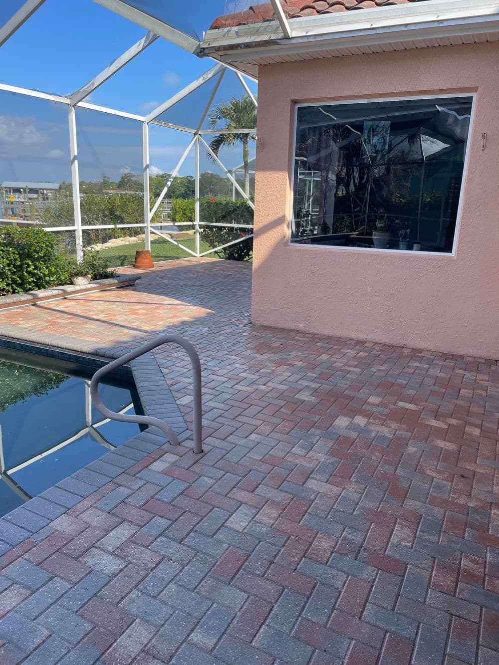 Modern paver patio by a pool with a house and natural scenery in the background.