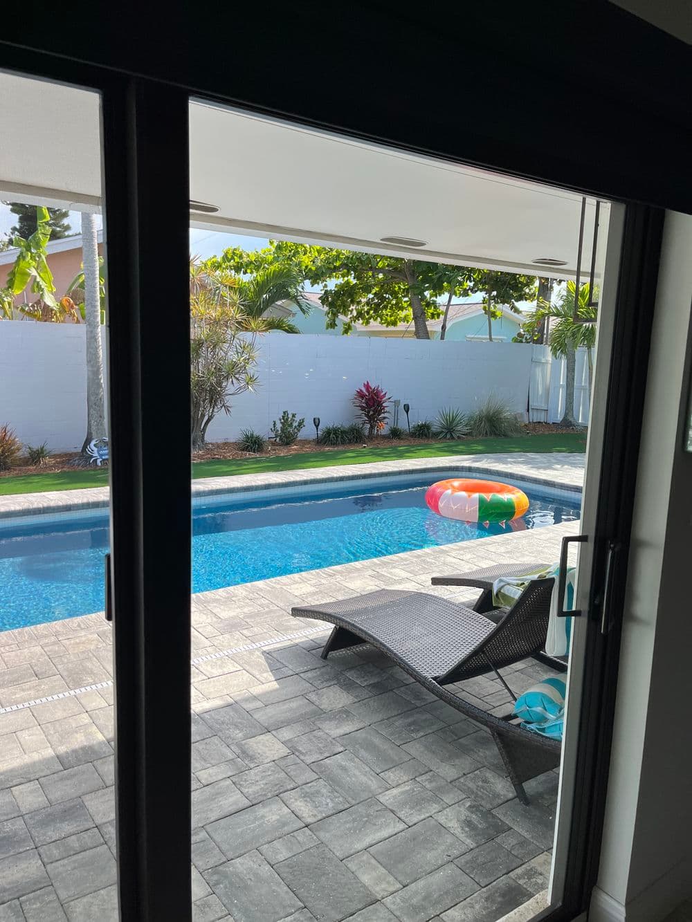View of a backyard pool with a floating toy and lounge chair, surrounded by lush greenery.