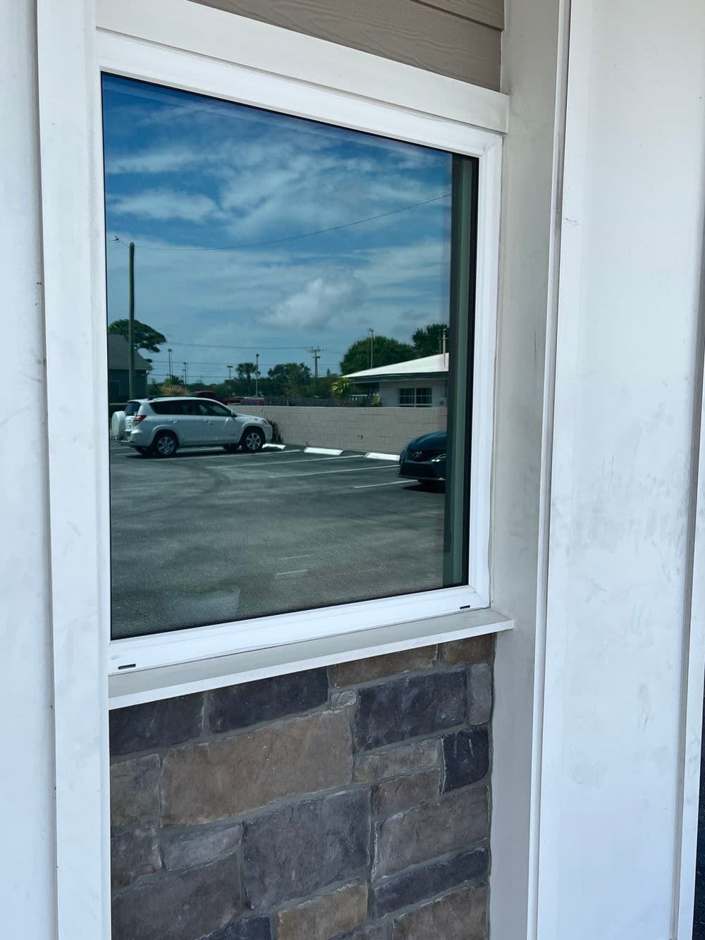 Modern window with reflection of cars and sky, framed by stone and siding.