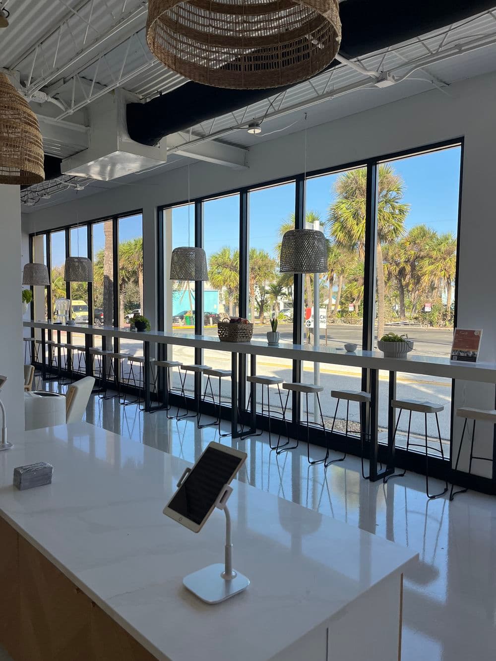 Bright modern café interior with large windows, bar seating, and woven pendant lights.