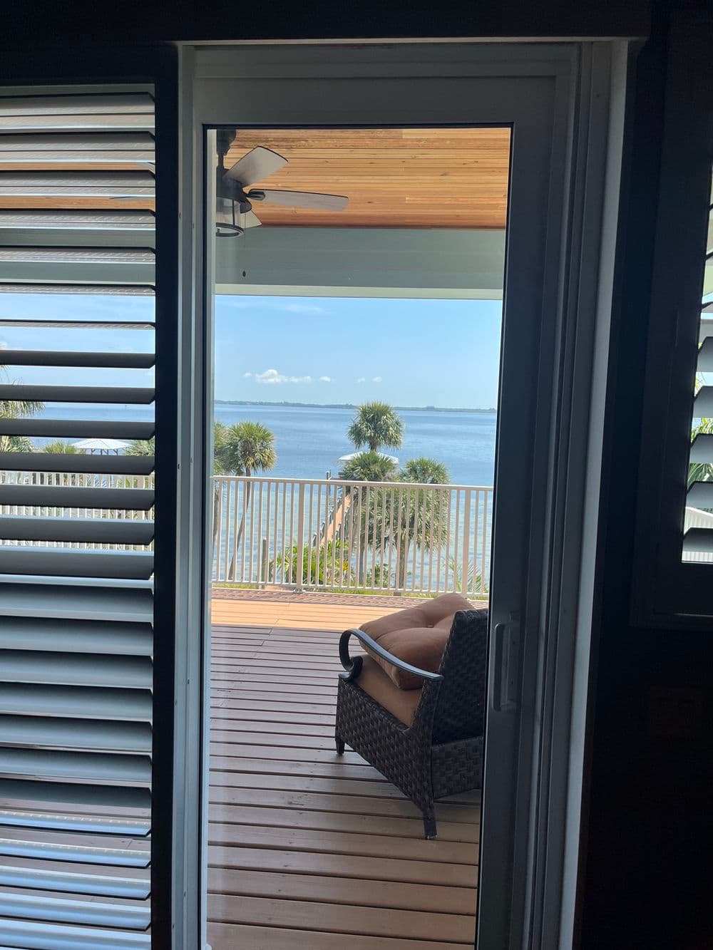 View from a door showcasing a patio with a chair overlooking a serene water scene.
