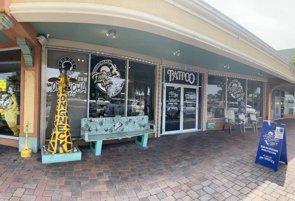 Tattoo shop storefront with colorful signs and a giraffe sculpture outside.