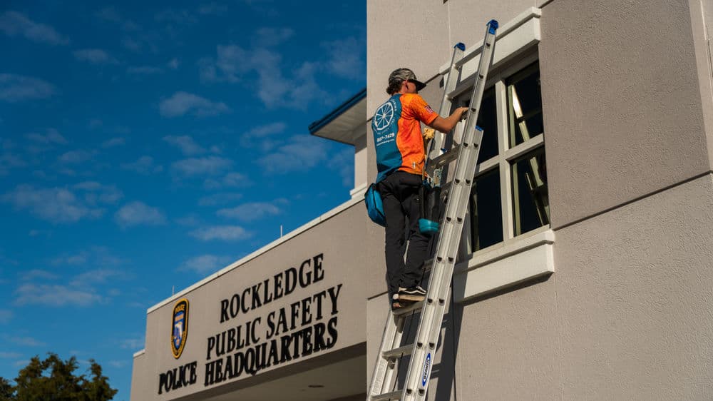 Worker using a ladder to clean windows at Rockledge Public Safety Police Headquarters.